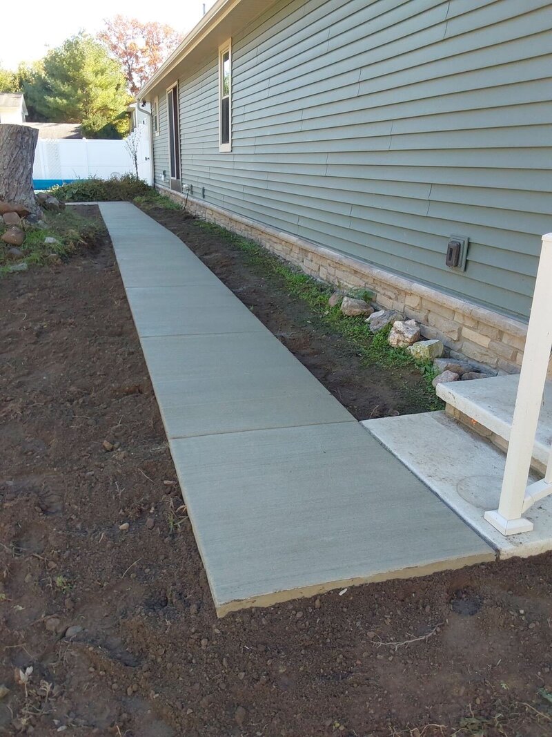Straight broom-finish concrete side walkway with freshly backfilled edges beside a home in Osceola, IN
