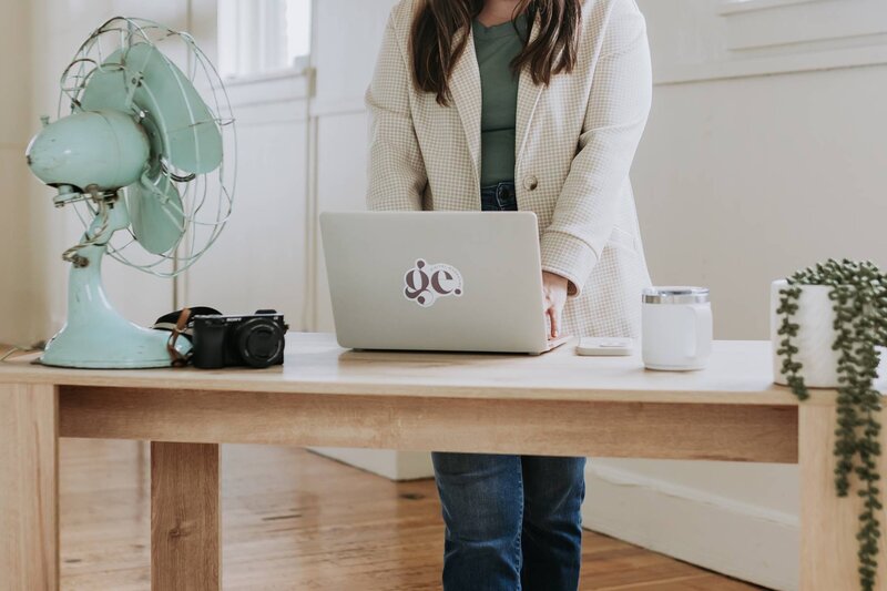McKenna Fahrenbruch, founder of Graceful Exposure Media, standing and typing on her laptop with branded logo visible—representing professional social media management, digital marketing, and content creation services.
