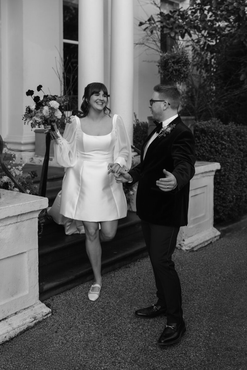 A couple pose with the bride raising the bouquet in the air at their luxury wedding ceremony in the cotswolds