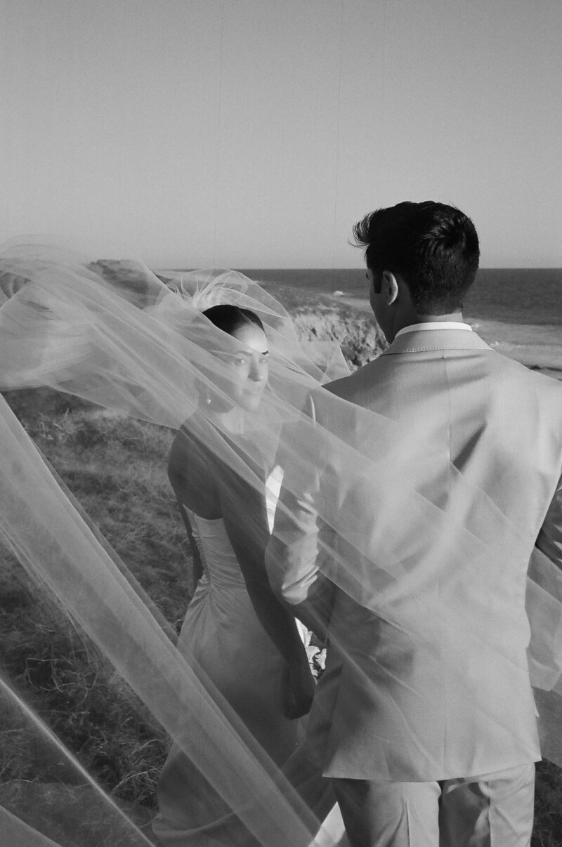 bride looking at me through a windswept veil with the ocean in the distance 