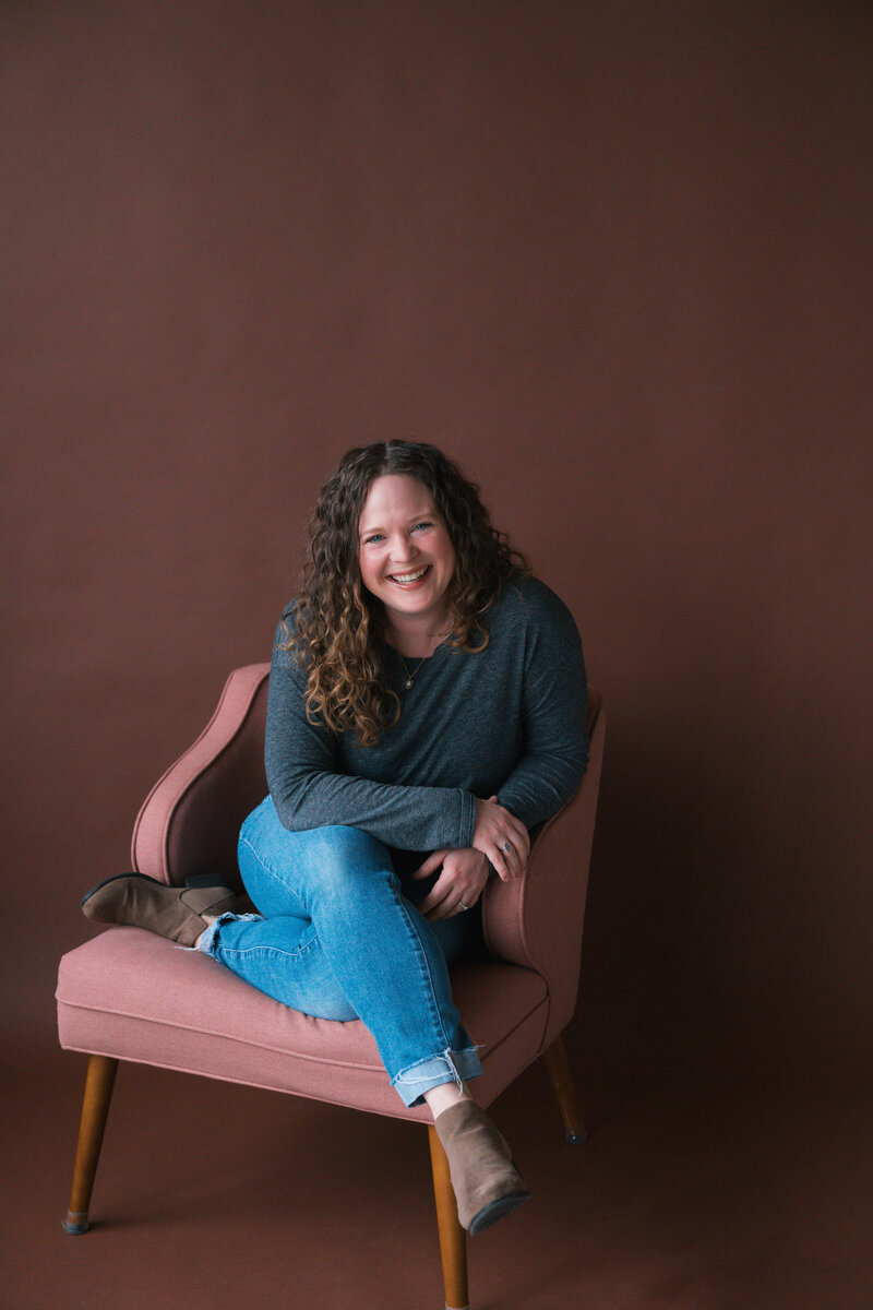 Becky Langseth, Seattle Birth Photographer, is smiling while sitting on a pink chair