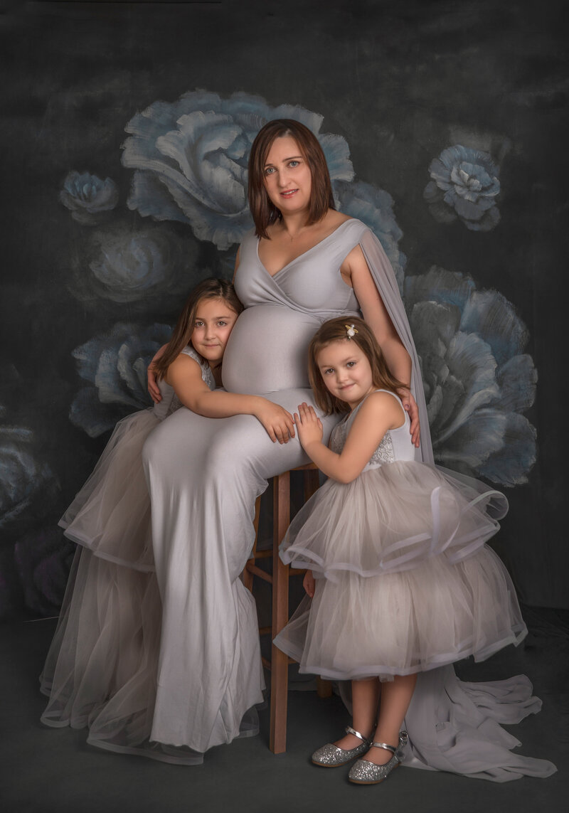 : "Pregnant mom in a beautiful fine art maternity session, surrounded by her daughters, captured in a timeless and elegant maternity portrait in Ottawa."