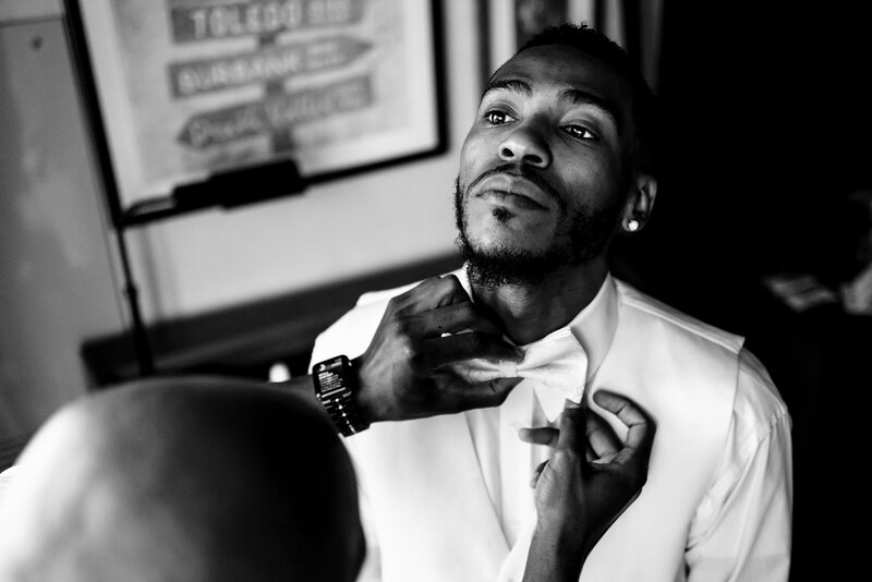 a groom looking up as his friend helps adjust his tie
