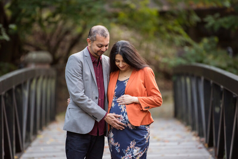 A couple looking at their unborn child with joy standing at a bridge.