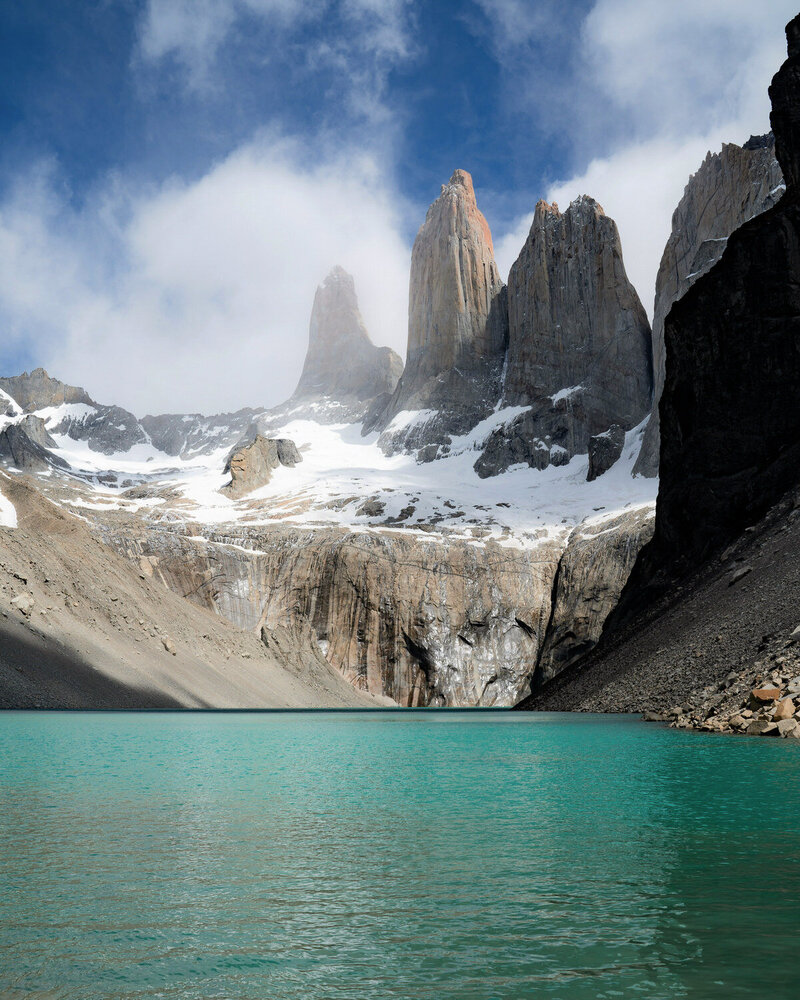 Emerald green alpine lake with tall mountains and clouds in the sky