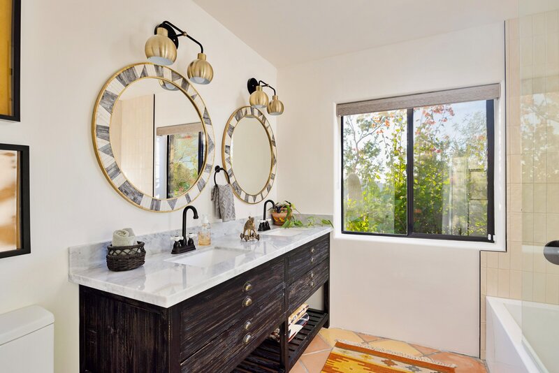 Modern-rustic spacious guest bathroom with a marbled-topped double vanity and geometric patterned mirrors. 