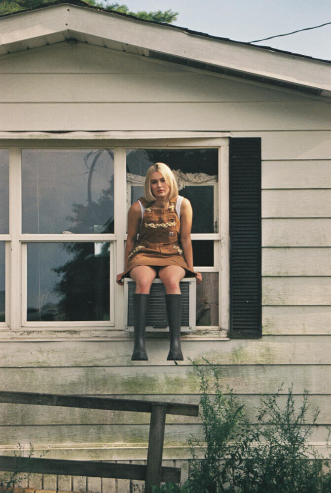 A woman sits on an old window air conditioning unit, representing an outdoor styled photoshoot. 