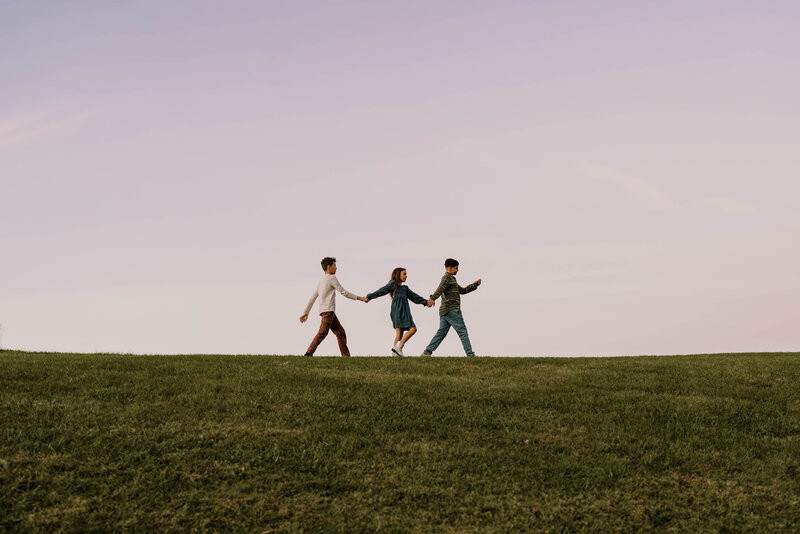 Three siblings walking on top of a big hill at sunset