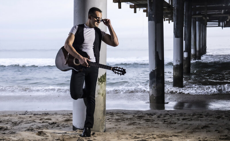 Music Artist Portrait  Eddie Garbarino standing under pier holding guitar