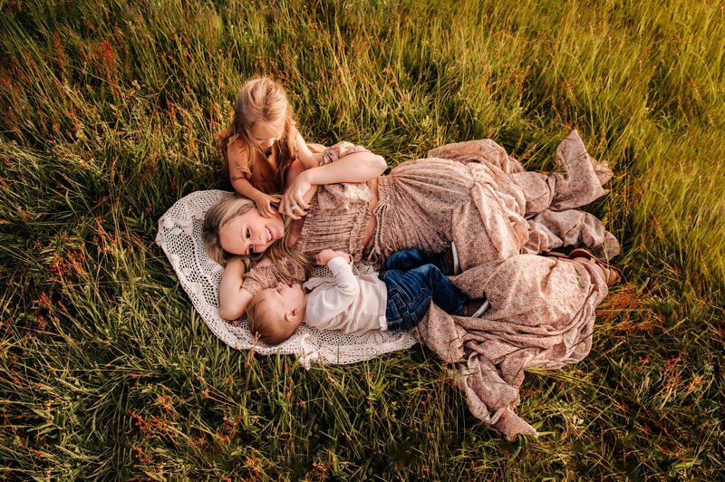 Mother laying on a blanket cuddling her kids in the grass