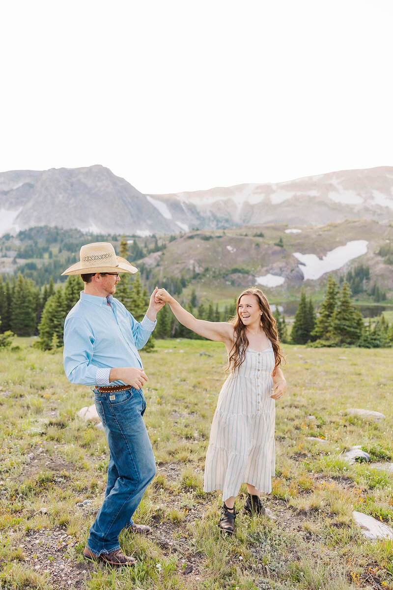 Joyful couple dancing in the breathtaking Snowy Range Mountains near Laramie, Wyoming, surrounded by lush greenery and stunning peaks, capturing the essence of love and adventure in outdoor photography.