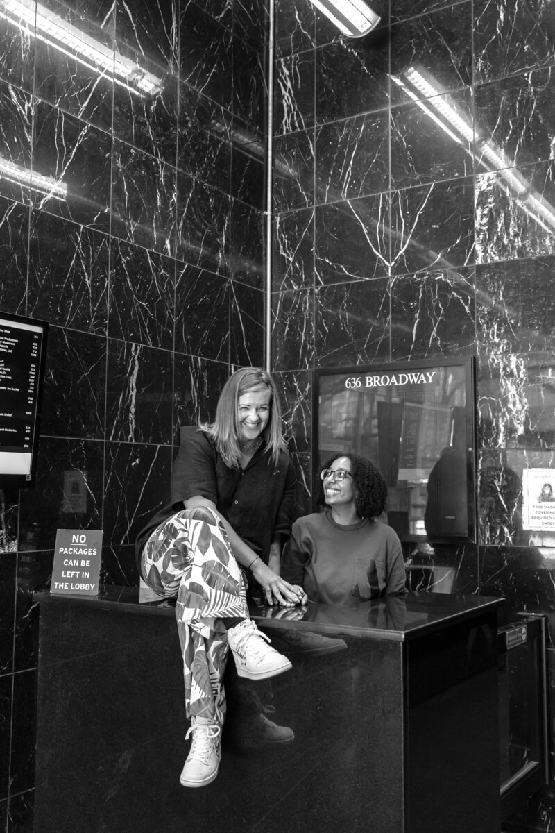 Dr. Nicole Harkness, acupuncturist and owner of Haystack Acupuncture, sits on desk smiling at camera alongside receptionist on 636 Broadway, NYC.