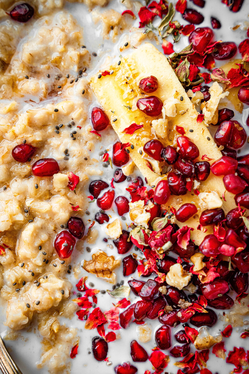 A close up shot on some oatmeal with pomegranate seeds, bananas and walnuts on top