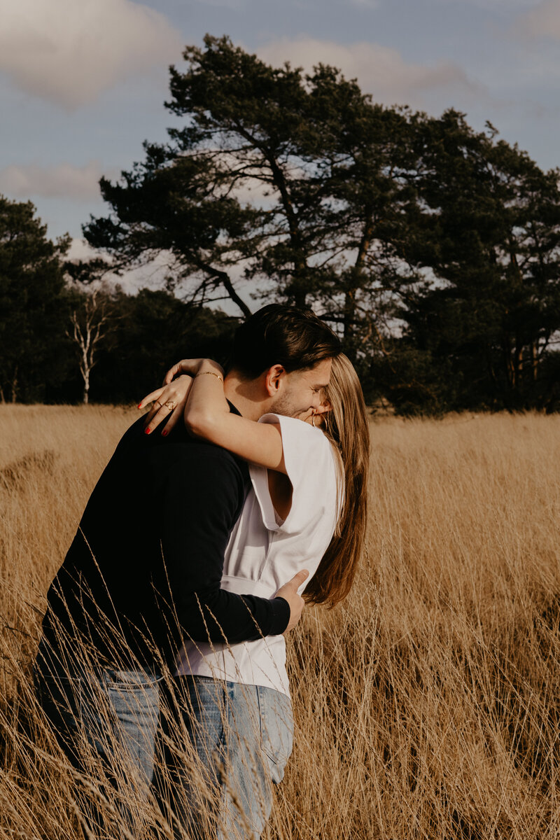 Een man en vrouw omarmen elkaar in een uitgestrekt veld, omringd door natuur en een gevoel van verbondenheid.