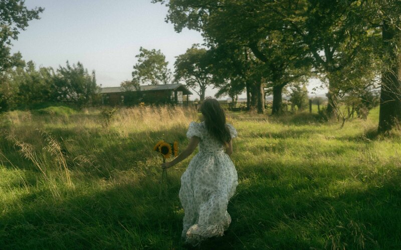 Woman running with a sunflower, captured in a dreamy, whimsical photoshoot, filled with natural light and soft, romantic vibes that evoke beauty and freedom
