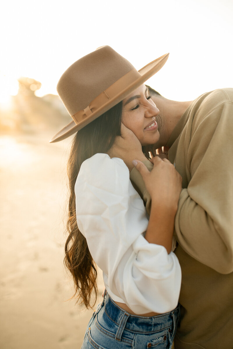 husband kissing wife on the neck during sunrise at laguna beach