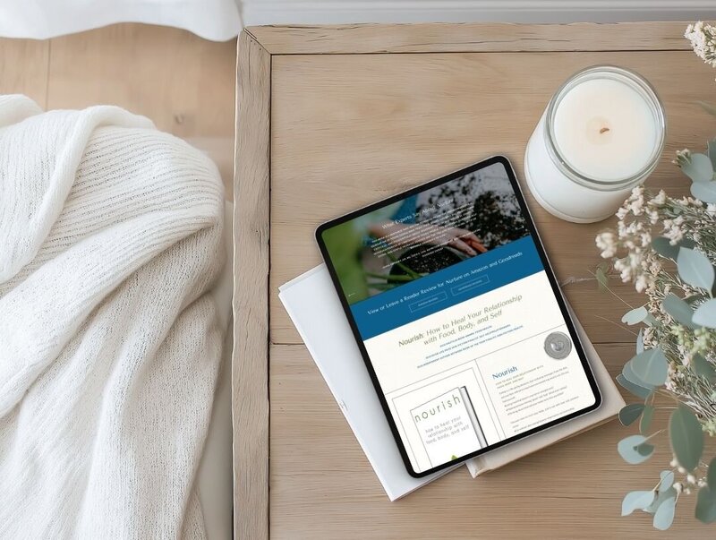A tablet on a table beside a candle and a book, creating a cozy atmosphere for a nutritionist's website.
