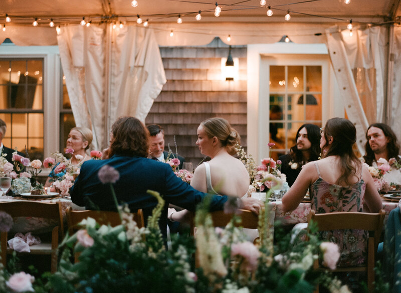 Film photo of a candlelit dinner scene at a Cape Cod micro wedding, with the bride and groom seated at a floral-filled table surrounded by loved ones — documented by a film wedding photographer.