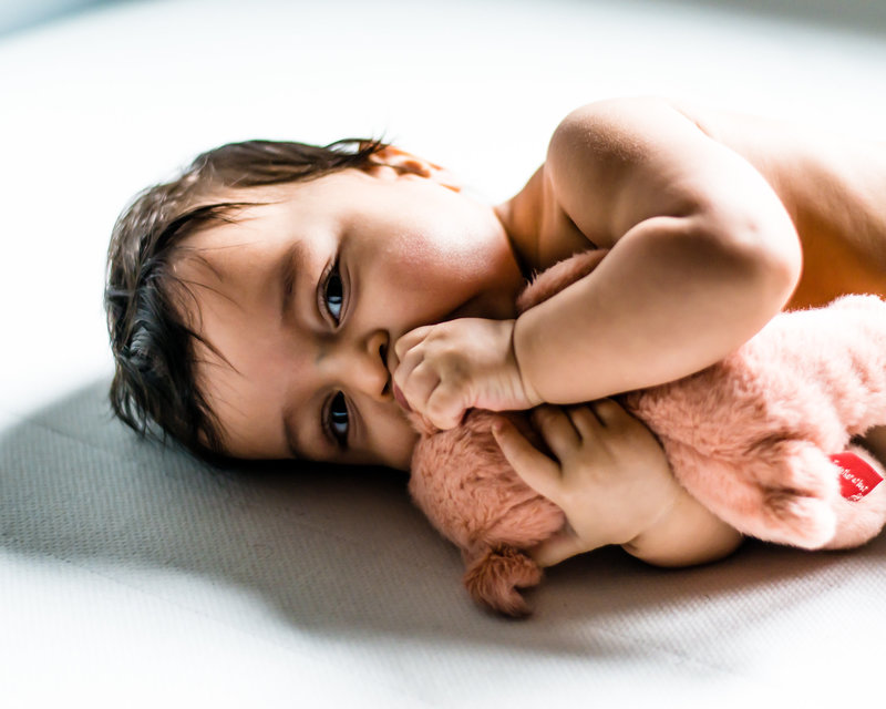 Baby chewing on ear of plush toy