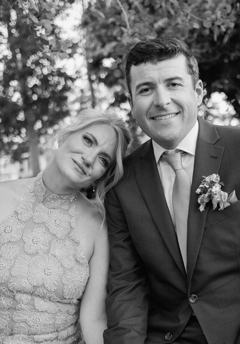 bride and groom lean on each other a softly smile at the camera