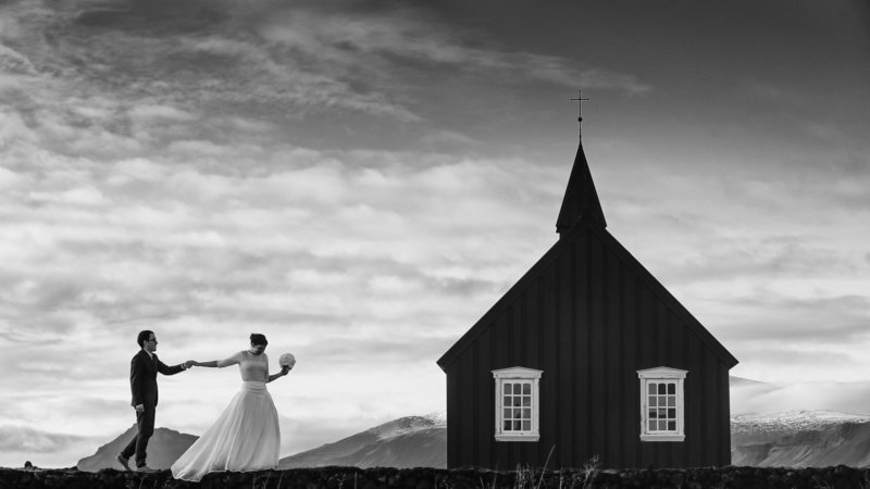 A wedding couple walks near the Black church in Iceland.