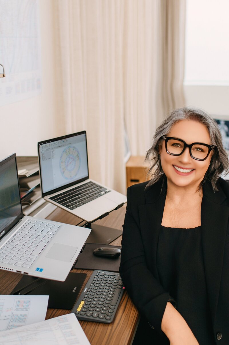 Astrocartographer Kristine Odegard in her office with two laptops and astrocartography maps