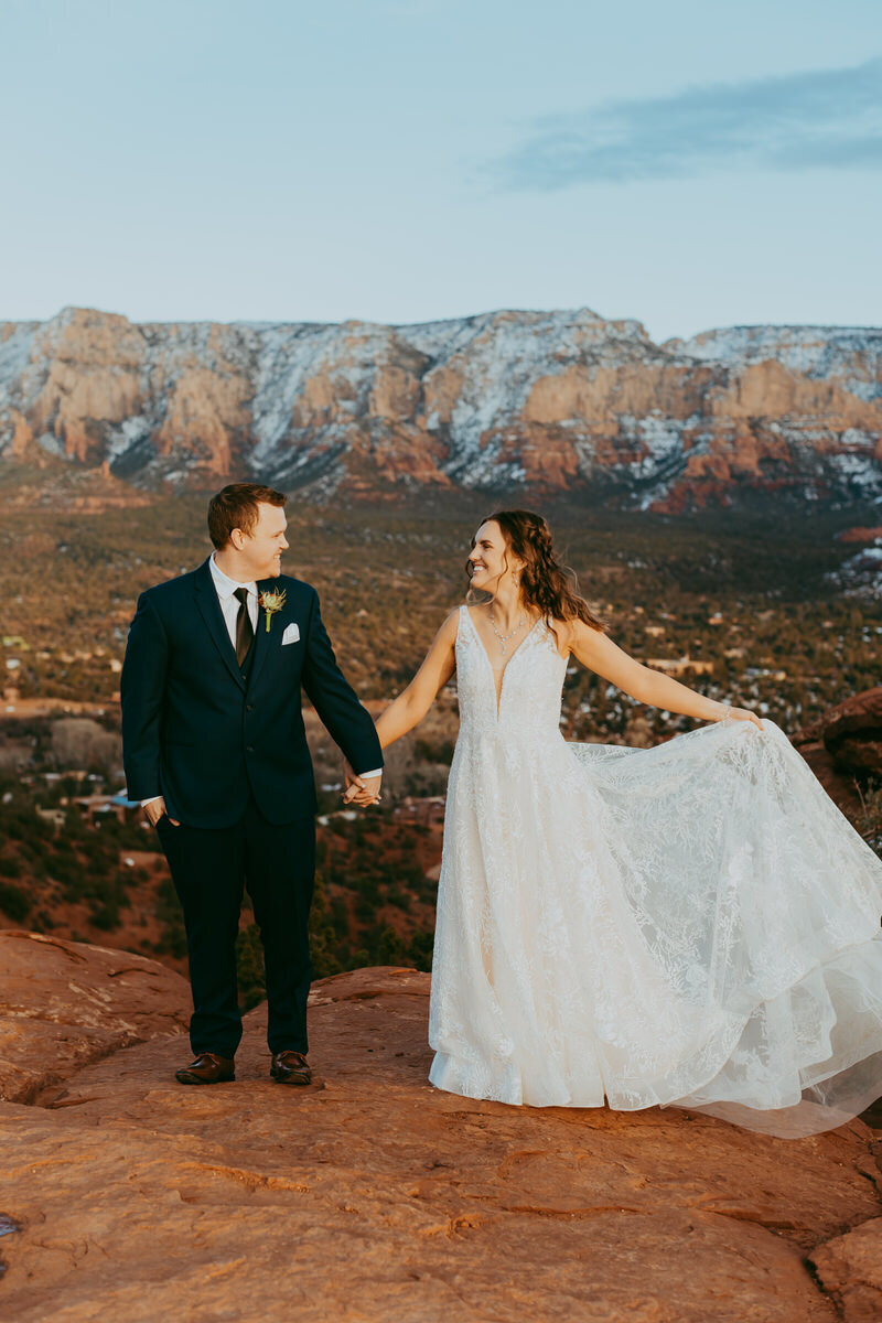 man and woman hold hands with snow covered peaks behind them in sedona