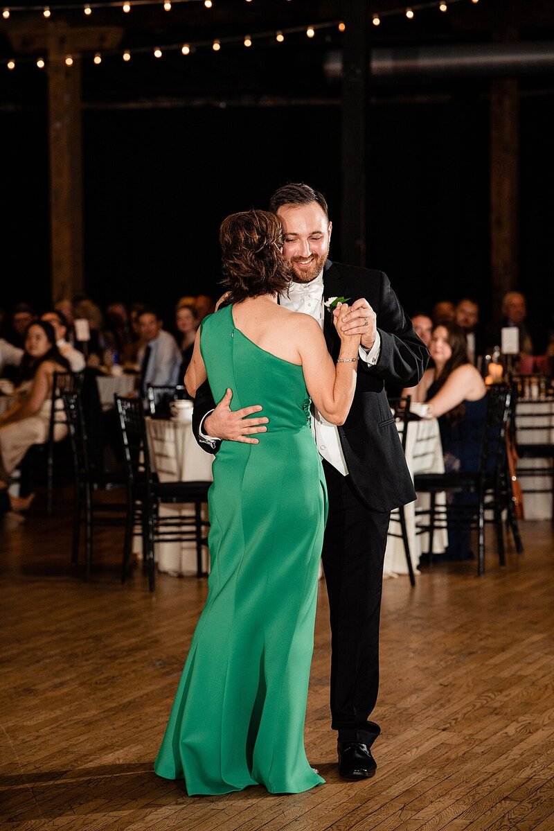 Groom dancing with his mom during the reception, she is a in a hunter green dress