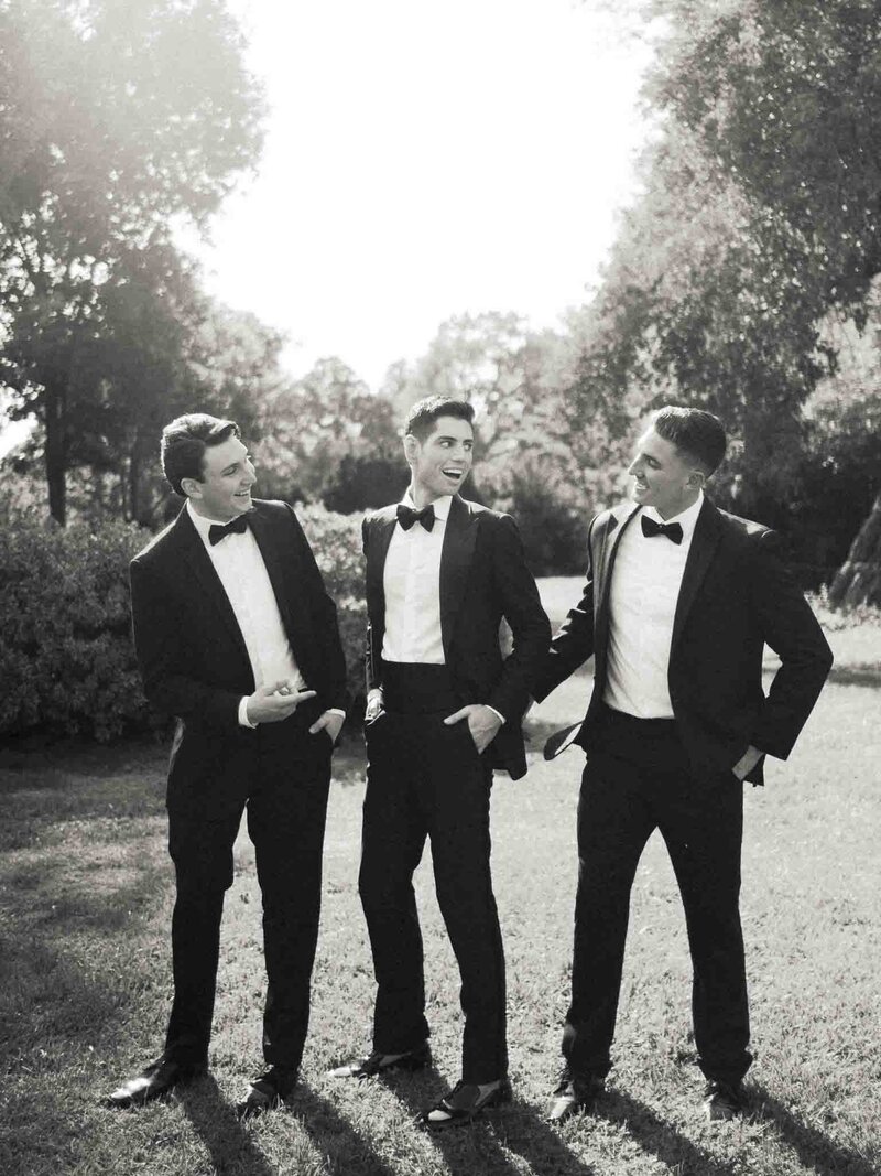 black and white photo of a groom and two groomsmen sharing a laugh in beautiful back light