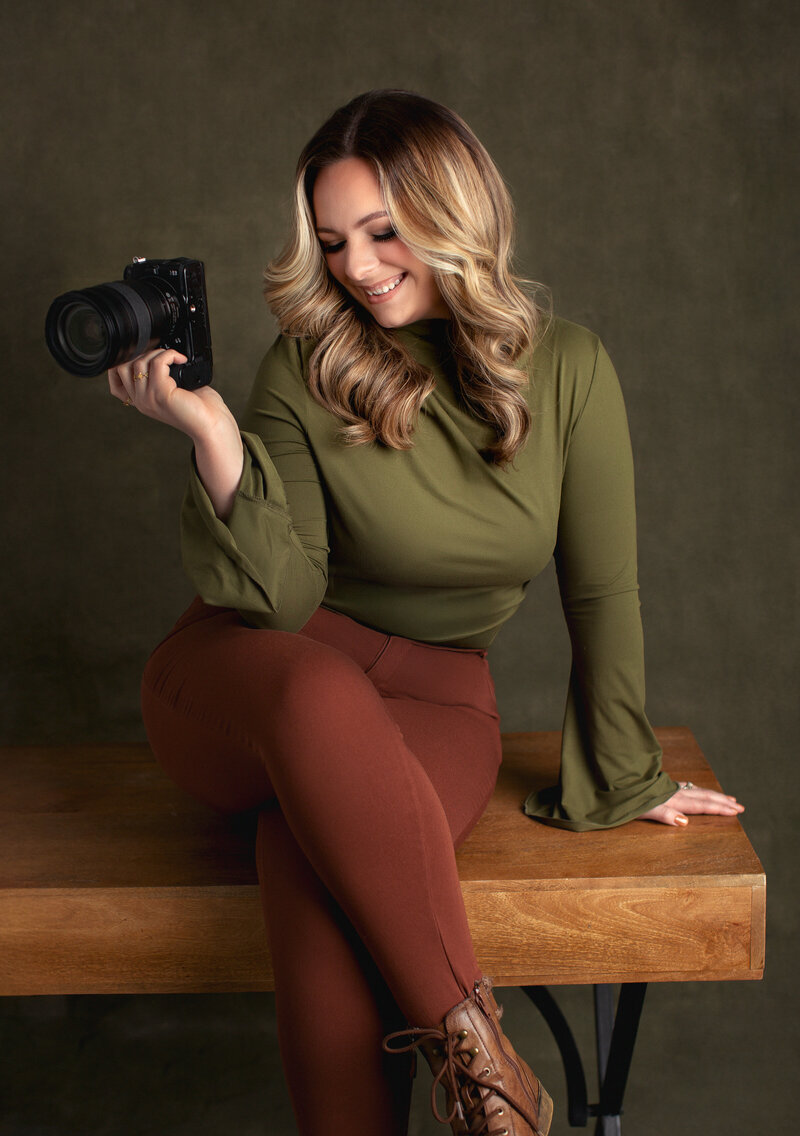 The owner of Kara Reese Photography poses in a black turtleneck with a Nikon camera in our Waukesha studio.