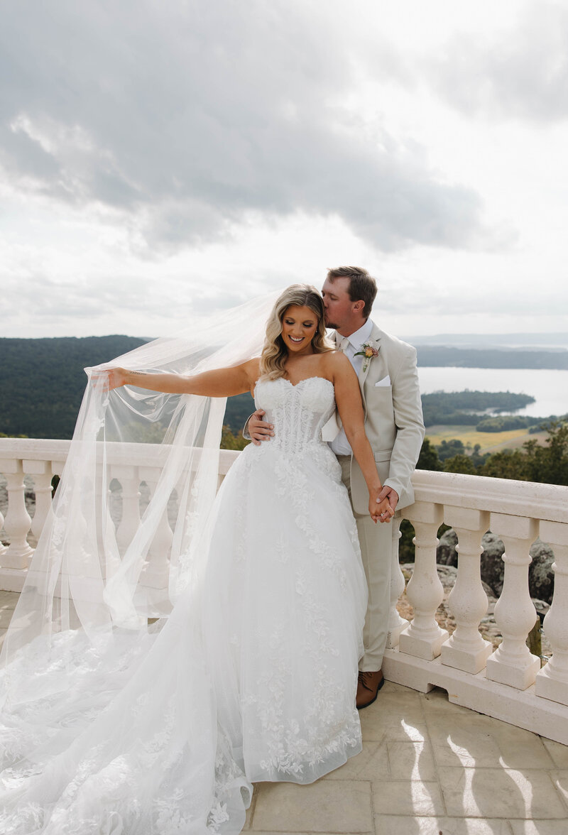 Bride Playing with her veil while her groom kisses her temple at Stone Haven Wedding Venue