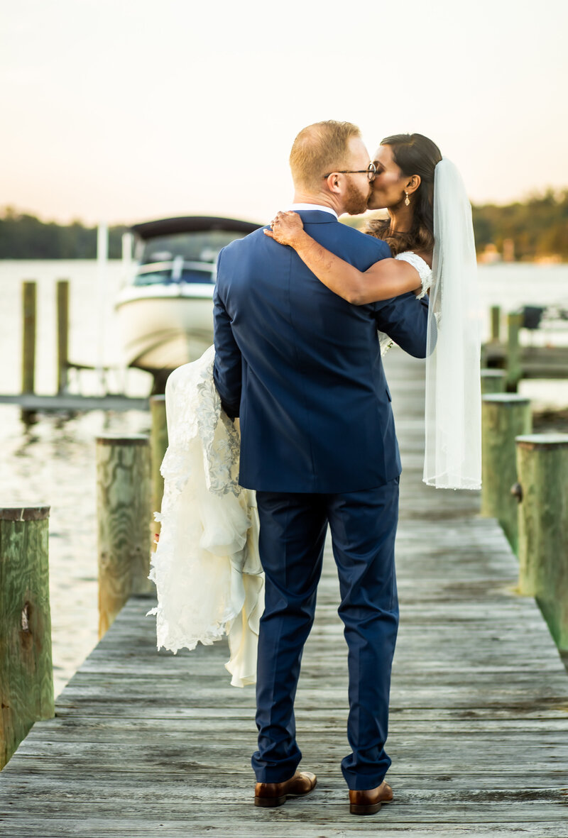 Groom holds bride, kissing her on the pier at a private wedding held in Annapolis Maryland