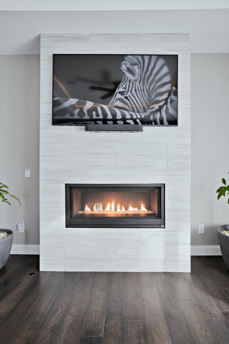 A custom-designed fireplace set on rich wood flooring, with a stylish TV or art piece hanging above. The perfect blend of functionality and design, this fireplace adds warmth and elegance to the living space.