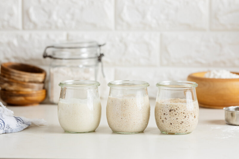Sourdough starter jars at The Rollin’ Pin Bakery, showing stages of natural fermentation and faith-inspired artisan baking.