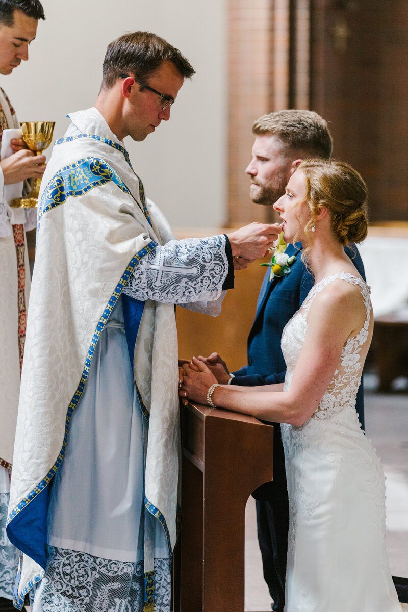 Bride and groom at kneeling bench taking mass from priest