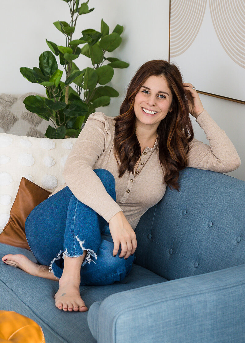 Woman with brown hair sitting on couch in a living room smiling