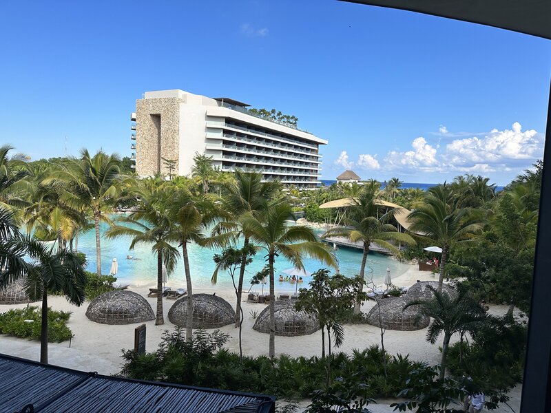 Lagoon-style pool surrounded by palm trees and thatched umbrellas at Secrets Moxché Playa del Carmen, a tropical luxury resort for destination weddings.