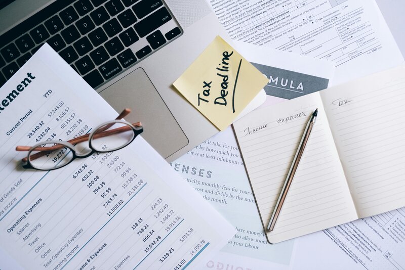 Close-up of financial documents, tax forms, and a sticky note labeled 'Tax Deadline' on a laptop keyboard"