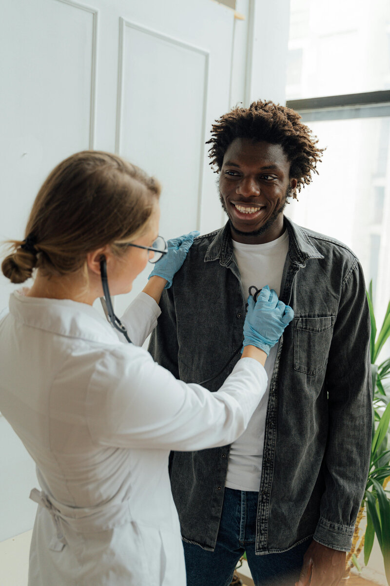 Female healthcare provider using a stethoscope to check a smiling male patient’s chest during a clinic visit.
