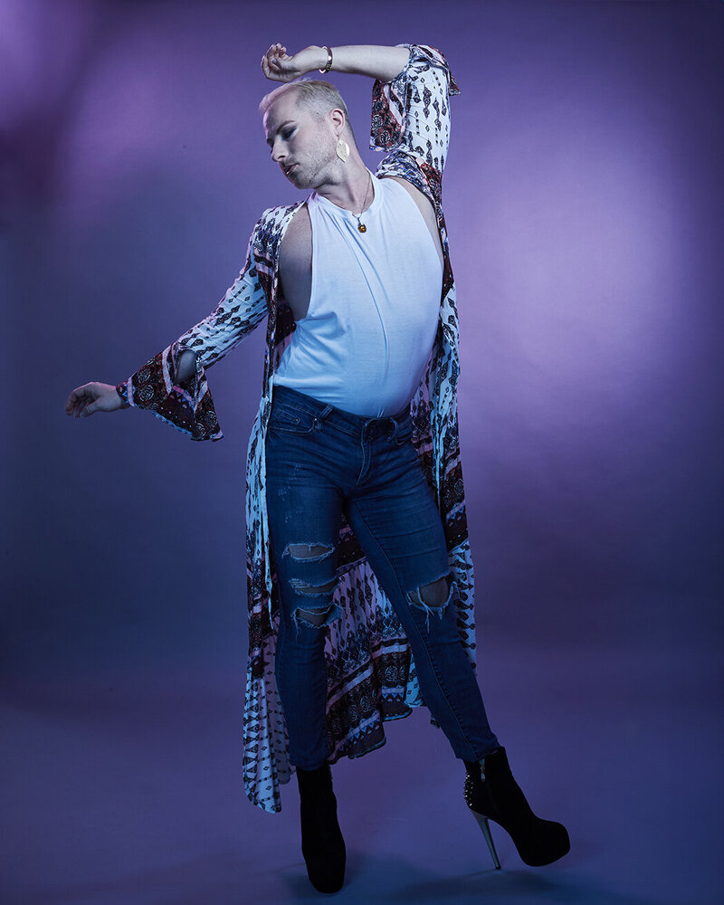 Creative studio portrait of Dain August gesturing gracefully in a sparkling blue outfit, highlighted by bold lighting effects.