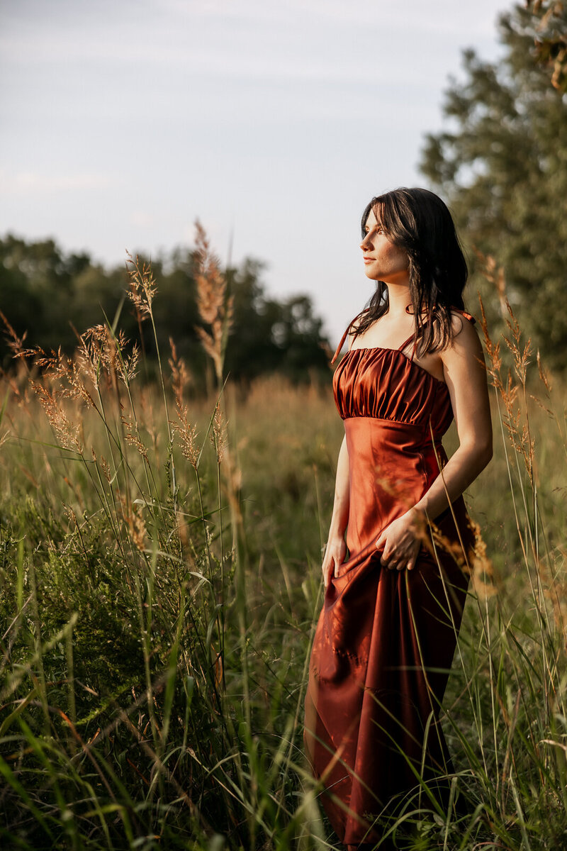 Sunset portrait of a high school senior wearing a gown in a field. 