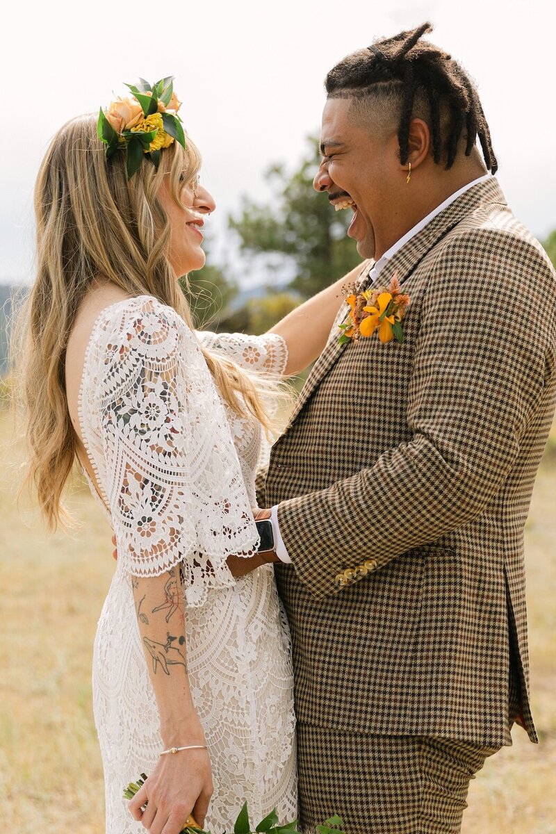 Bride and groom hiding playfully behind a white parasol with bouquet visible in a Colorado meadow – whimsical Colorado wedding photos