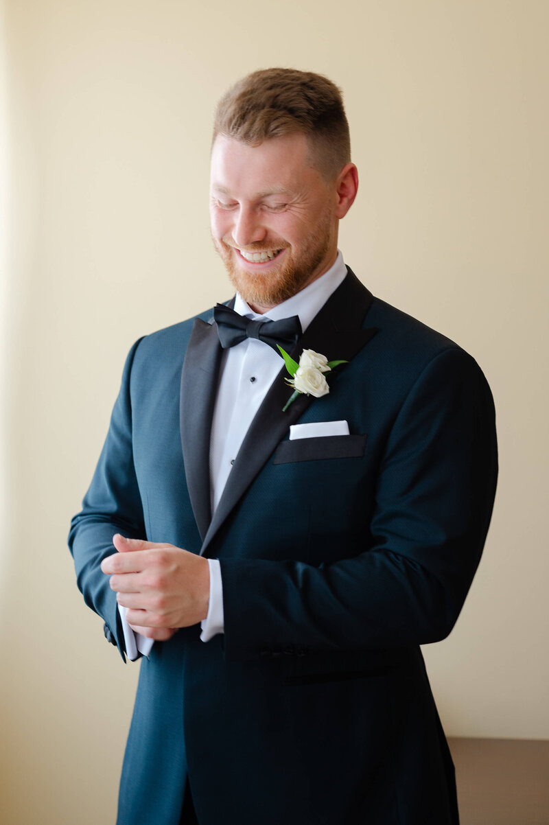 a groom in a black tux adjusting his cufflinks and smiling.  Captured by Ottawa wedding photographer JEMMAN Photography