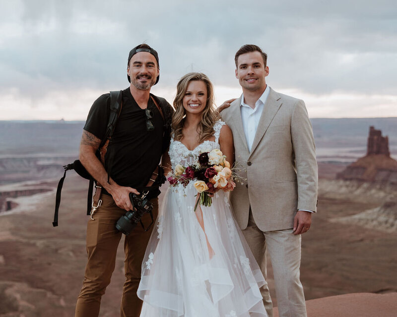 bride and groom and their photographer in the desert while smiling