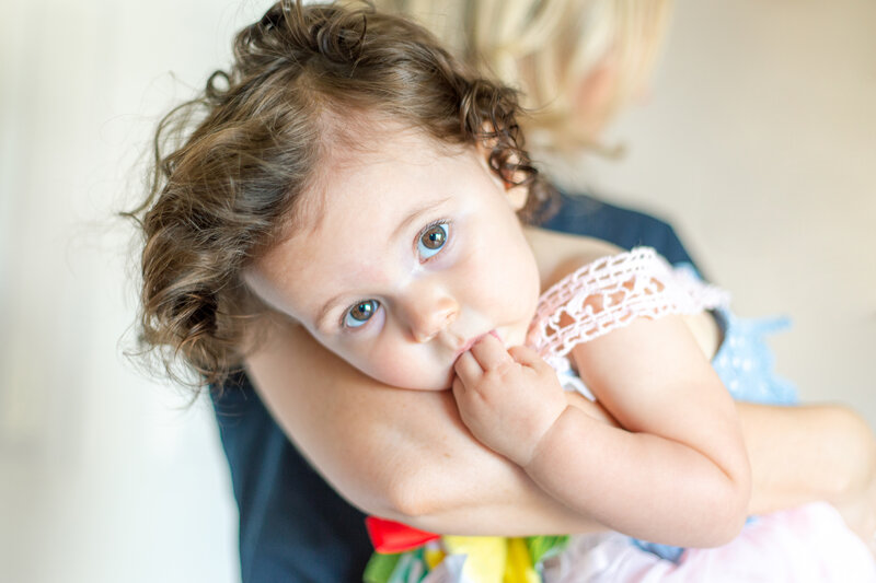 toddler girl looking at camera sucking on fingers