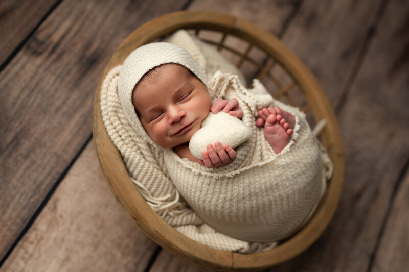 Sweet and simple—this smiling baby boy clutches a soft felt heart while wrapped in creamy textures and love.