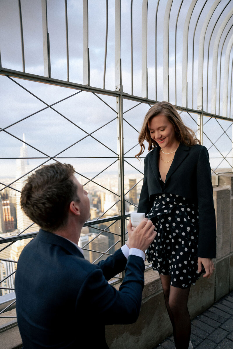 Romantic surprise proposal at the top of the Empire State Building with the NYC skyline in the background.