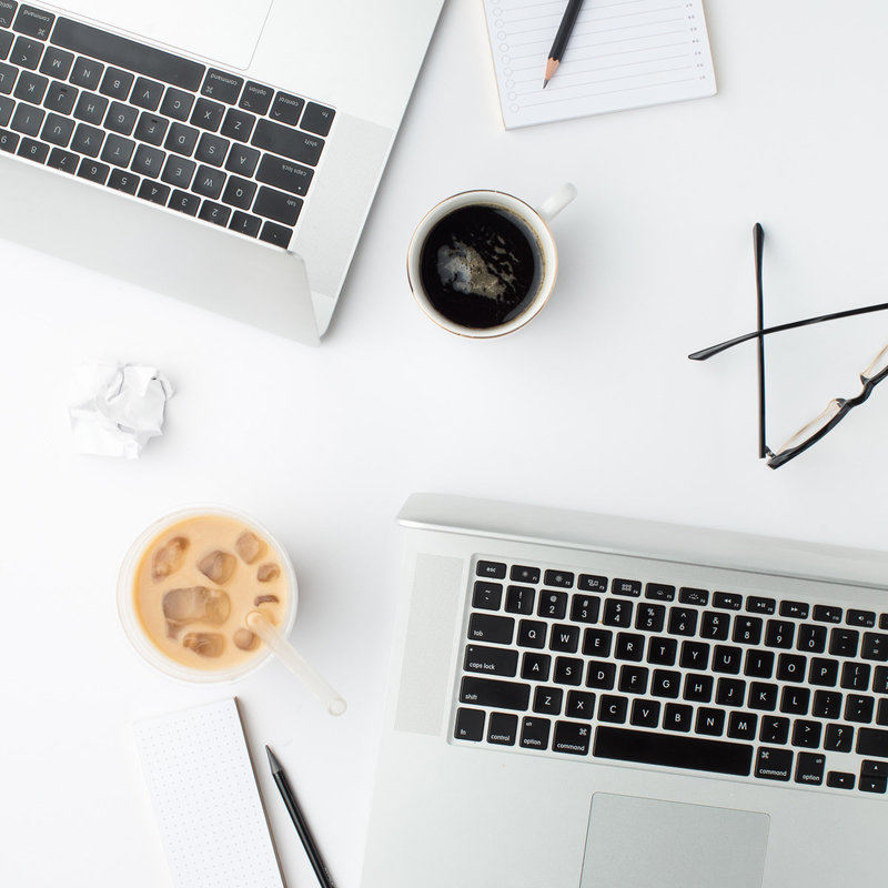 Computers on a desk with coffees, notebooks, and pencils