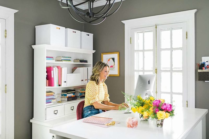 woman working at a desk in a light and bright white office space with pops of pink and yellow