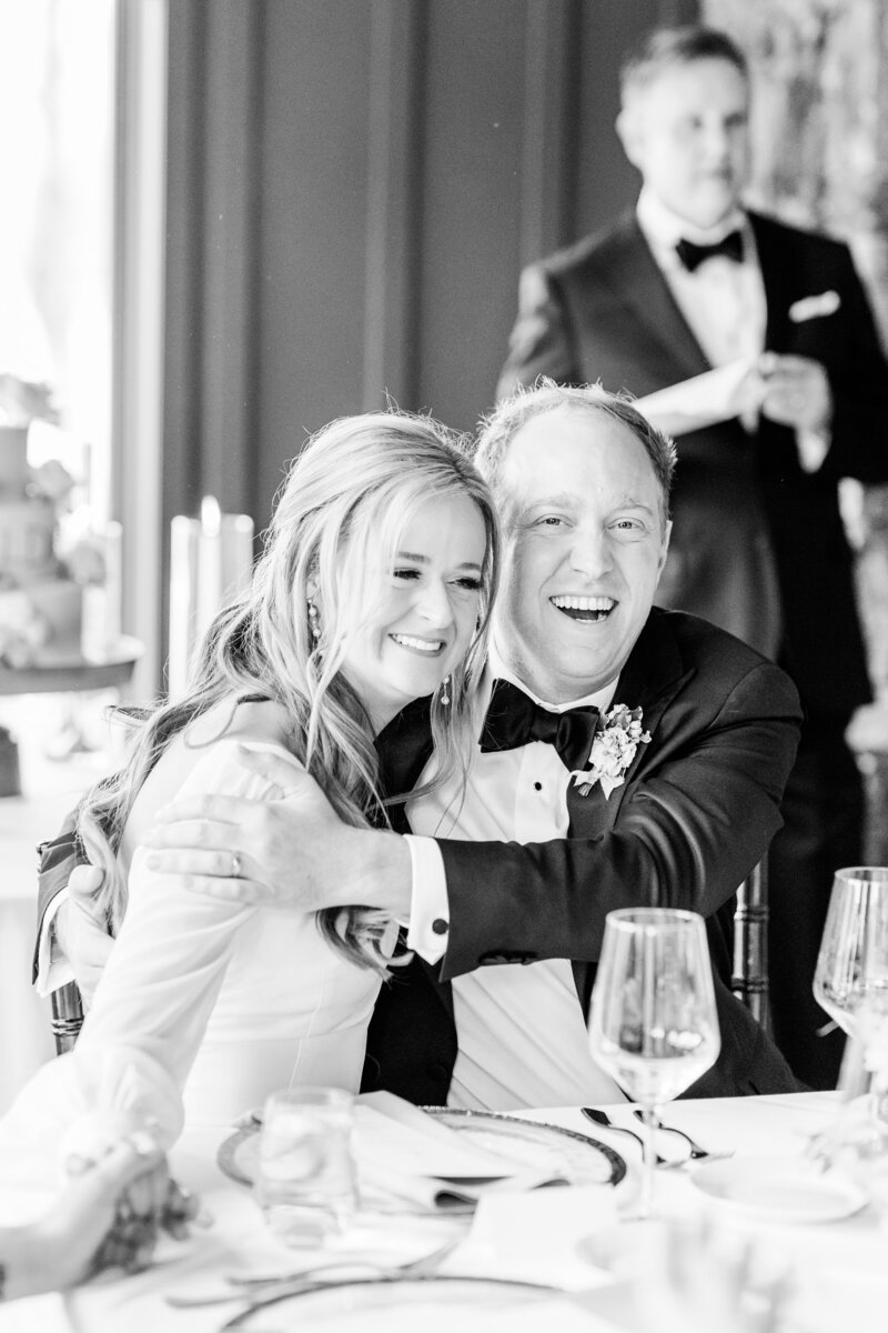 black and white photo of bride and groom laughing during toasts